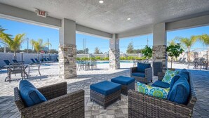 Un patio al aire libre con mobiliario de mimbre, piscina y palmeras.