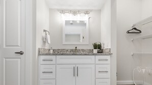 Une salle de bain avec des meubles blancs, un comptoir en granit, un lavabo, un miroir avec éclairage intégré et un porte-serviettes.