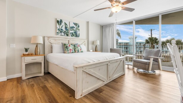 Une chambre à coucher comprenant un lit, des tables de chevet, un ventilateur de plafond et un balcon avec une chaise.