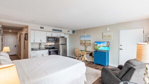 Une chambre comprenant un lit, un bureau, une chaise, un téléviseur et un coin cuisine.