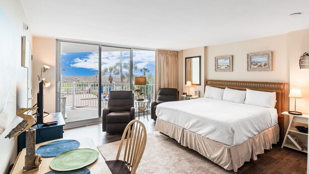 Une chambre d’hôtel avec un grand lit, deux fauteuils, un bureau avec une lampe et une vue sur l’extérieur.