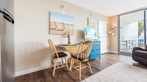 Un coin repas avec une table et des chaises en bois, un tableau représentant une scène de plage et un meuble bleu.