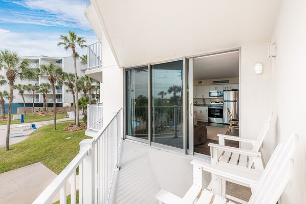 A balcony with white railings, a view of a pool, and a kitchen area visible through glass doors. - Sandcastle Condominiums Unit 117 (Port Aransas)