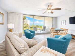 A hotel room with a balcony, a ceiling fan, a sofa, a chair, and a table.