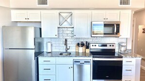A modern kitchen with stainless steel appliances, white cabinetry, and a granite countertop. - Sandcastle Condominiums Unit 202 (Port Aransas)