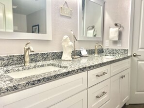 Un baño con encimera de granito, dos lavamanos, un perchero y un espejo.
