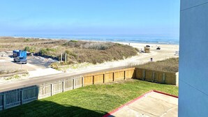 A balcony with a view of the beach, a wooden fence, and a blue dumpster. - Sandcastle Condominiums Unit 202 (Port Aransas)