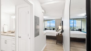 Een hotelkamer met een groot bed, een bureau met stoel, een klein tafeltje en uitzicht op de lucht door grote ramen.