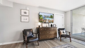 Een woonkamer met een televisie, twee stoelen, een houten dressoir en een groot raam.