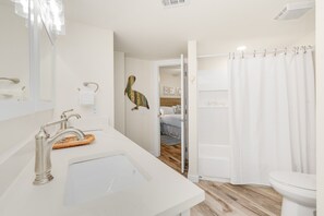 A bathroom with a white sink, a shower curtain, and a visible door leading to a bedroom. - Sandcastle Condominiums Unit 213 (Port Aransas)