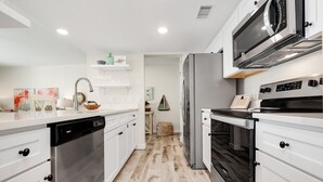 A modern kitchen with white cabinetry, stainless steel appliances, and a wooden floor. - Sandcastle Condominiums Unit 213 (Port Aransas)
