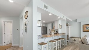A modern kitchen with a central island, bar stools, and a refrigerator. - Sandcastle Condominiums Unit 225 (Port Aransas)