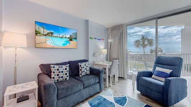 Un salon moderne avec un canapé, un fauteuil et un tableau représentant une scène de plage.