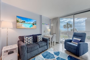 Un salon moderne avec un canapé, un fauteuil et un tableau représentant une scène de plage.