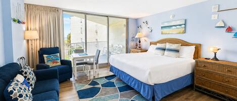 A hotel room with a bed, a desk, a chair, a sofa, a balcony with a view, and a dining area.