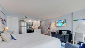 Une chambre d’hôtel moderne avec un grand lit, un canapé bleu foncé, une petite table à manger et un coin cuisine.
