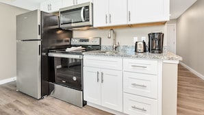 A modern kitchen with stainless steel appliances, white cabinetry, and a granite countertop. - Sandcastle Condominiums Unit 227 (Port Aransas)