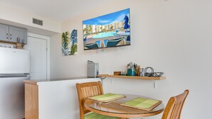 A modern kitchen with a white refrigerator, wooden cabinets, and a dining area with a glass table and wooden chairs.