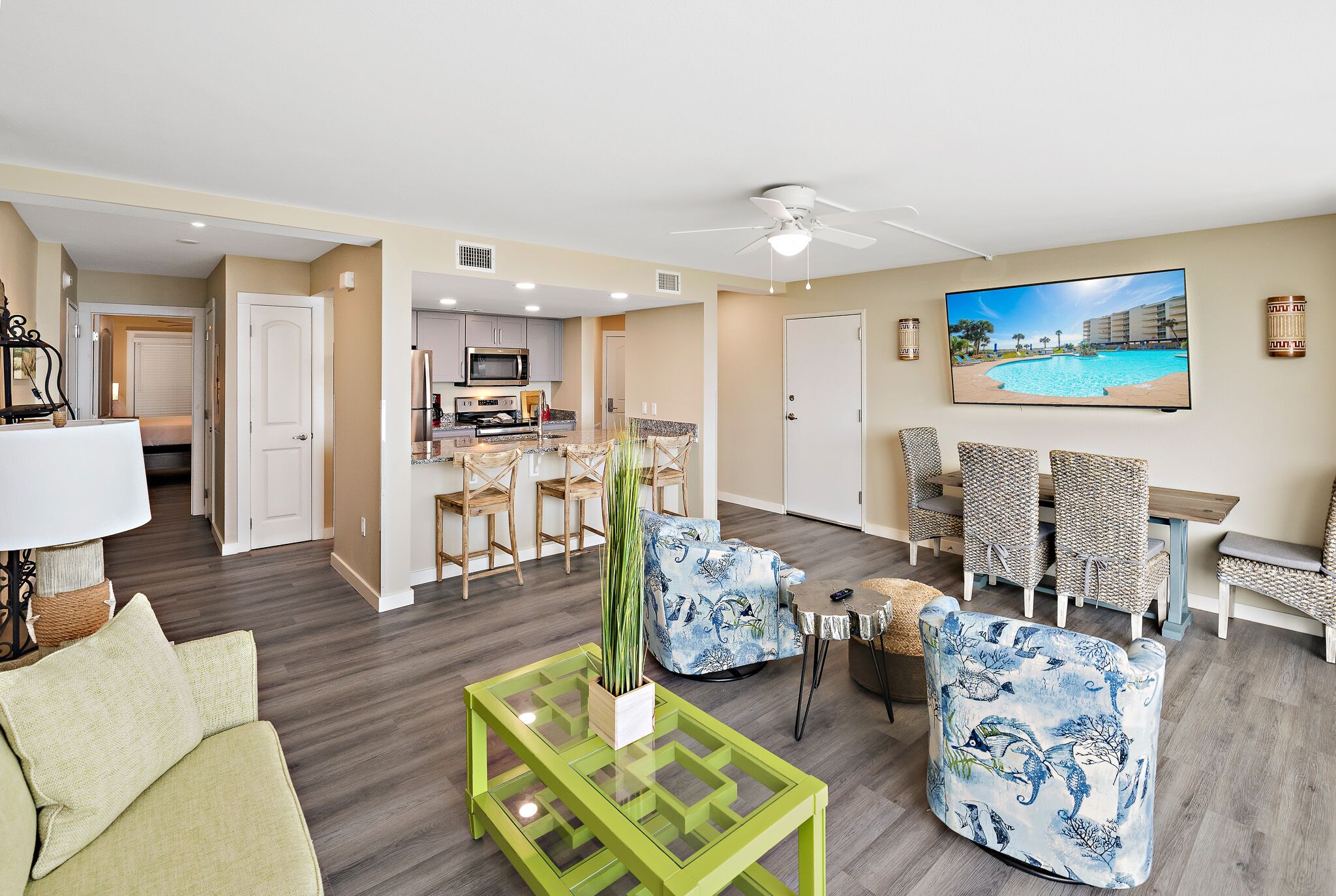 A spacious living area with a dining set, a TV, and a view of a pool.