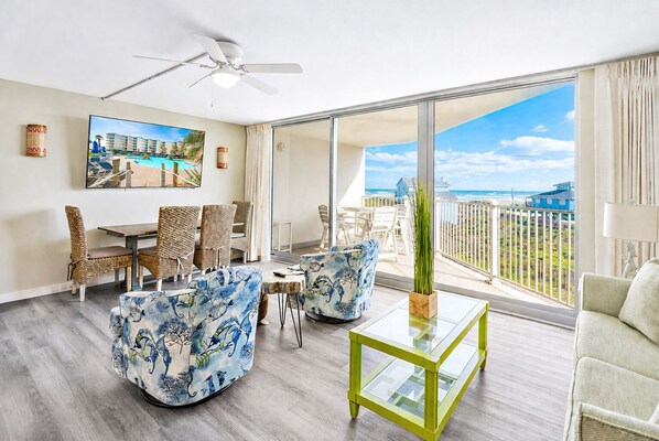 A spacious balcony with a view of the beach and ocean, furnished with wicker chairs and a table.