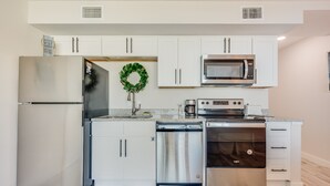 A modern kitchen with white cabinets, stainless steel appliances, and a decorative wreath on the countertop. - Sandcastle Condominiums Unit 235 (Port Aransas)