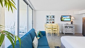 Ein modernes Zimmer mit einem blauen Sofa, einem Esstisch mit Stühlen, einem Fernseher, einer Kommode und einem Bett.