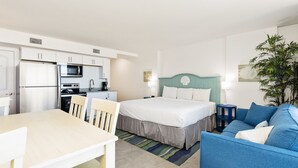 Ein kompaktes Hotelzimmer mit Küchenzeile, einem Bett mit Türkis-Kopfteil, einem blauen Sofa und einem Esstisch mit Stühlen.