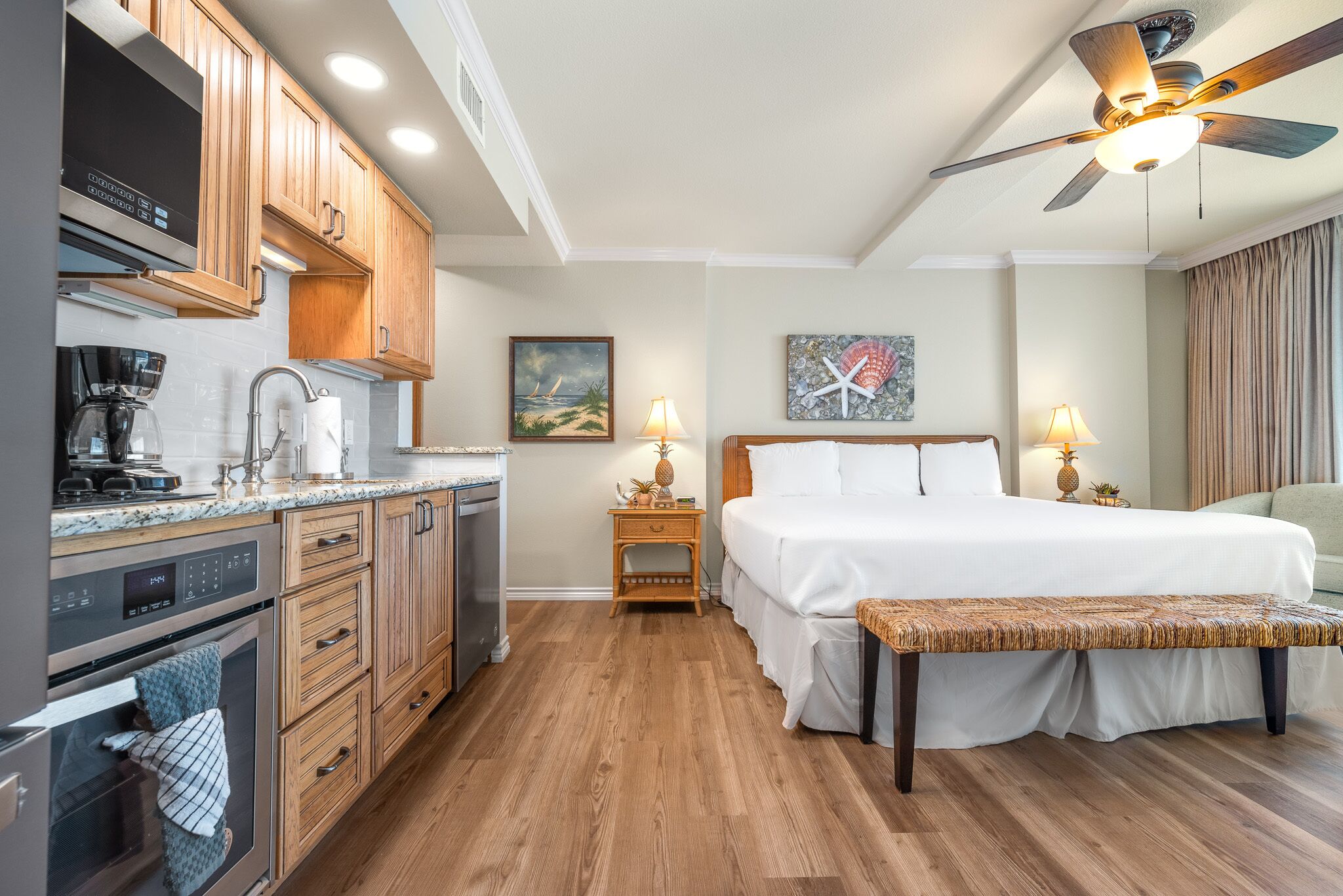 A hotel room with wooden cabinets, a bed, a ceiling fan, and a painting on the wall.