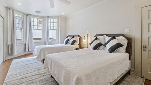 A bedroom with two beds, a ceiling fan, and a large window.