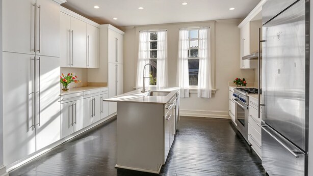 A modern kitchen with white cabinetry, a central island, stainless steel appliances, and a window with sheer curtains.