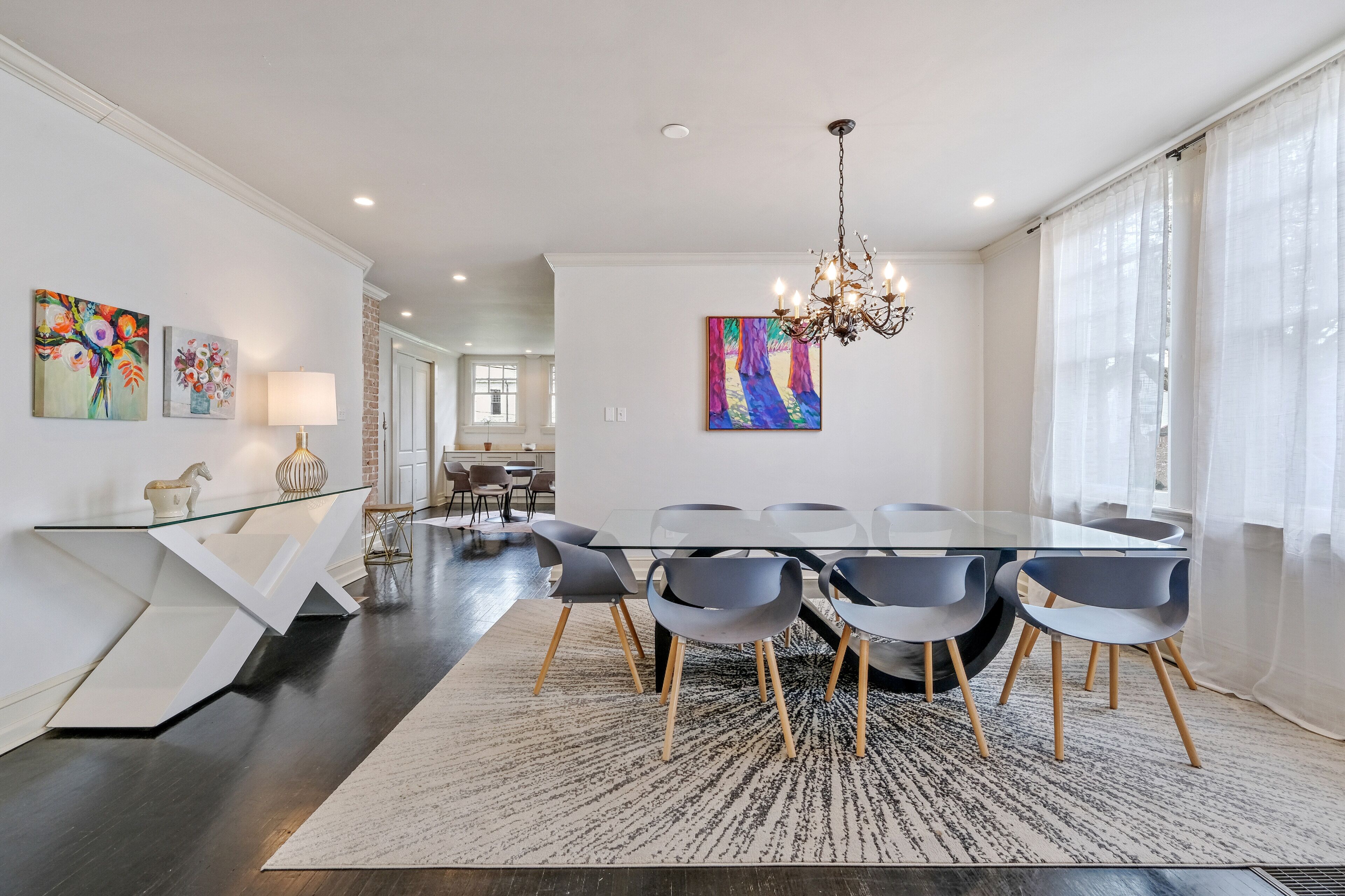 Un espace repas moderne avec une table en verre, des chaises grises et un lustre.