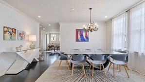 A modern dining area with a glass table, grey chairs, and a chandelier.
