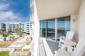 Un balcó amb cadires Adirondack blanques, una zona de piscina amb gandules i ombrelles, i vista d'un edifici d'un complex turístic amb múltiples balcons i palmeres.