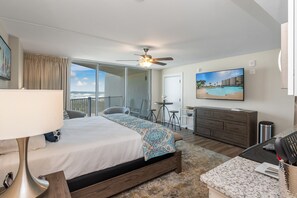 A hotel room with a bed, a desk, a TV, and a balcony with a view of the ocean. - Sandcastle Condominiums Unit 310 (Port Aransas)