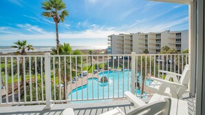 Un balcon donnant sur une piscine, des palmiers et un bâtiment en arrière-plan.