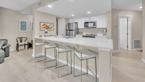 A modern kitchen with white cabinets, stainless steel appliances, and a bar area with stools.