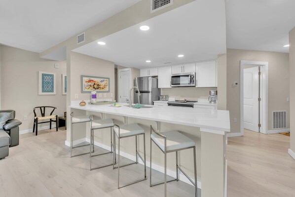 A modern kitchen with white cabinets, stainless steel appliances, and a bar area with stools. - Sandcastle Condominiums Unit 320 (Port Aransas)