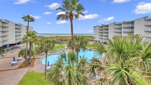 A resort with a swimming pool, palm trees, and beachfront balconies.