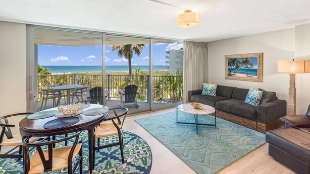 A room with a balcony, a dining table, a sofa, and a painting.