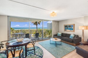 A room with a balcony, a dining table, a sofa, and a painting. - Sandcastle Condominiums Unit 320 (Port Aransas)