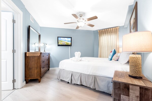Une chambre à coucher avec un lit, un ventilateur de plafond, une télévision, une commode et une lampe.