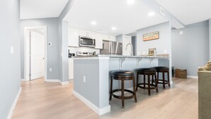 Una cocina moderna con armarios blancos, electrodomésticos de acero inoxidable y una zona de bar con taburetes.