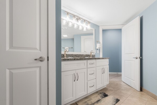 Une salle de bain moderne avec des meubles blancs, un comptoir en granit et un grand miroir avec éclairage intégré.