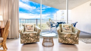 Un balcón con dos sillones y una mesa de vidrio, con vistas a un edificio y un cielo despejado.