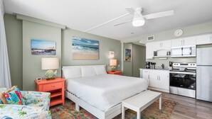 A hotel room with a bed, a small desk, a chair, a kitchenette, and a ceiling fan. - Sandcastle Condominiums Unit 328 (Port Aransas)