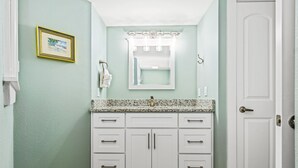 A bathroom with a white vanity, a sink with a mirror above it, and a framed picture on the wall. - Sandcastle Condominiums Unit 328 (Port Aransas)