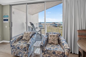 Un balcon avec vue sur la plage, deux chaises à motifs nautiques, une table et une pancarte sur laquelle on peut lire : « Bienvenue à la plage ».