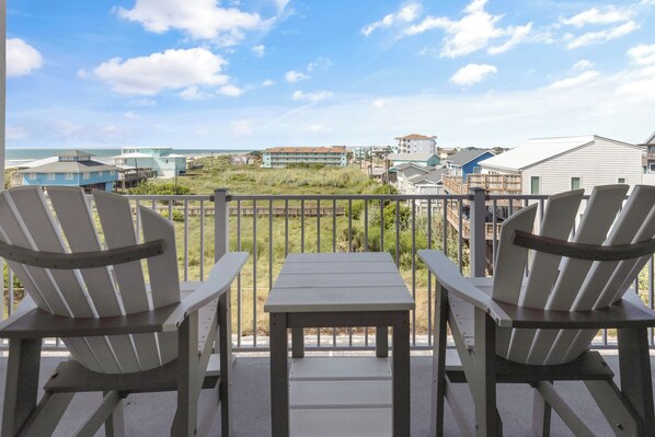 A balcony with two Adirondack chairs and a small table, overlooking a beach and buildings. - Sandcastle Condominiums Unit 332 (Port Aransas)