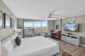 Une chambre d’hôtel avec un grand lit, une télévision, un balcon avec des chaises et une vue sur la plage.