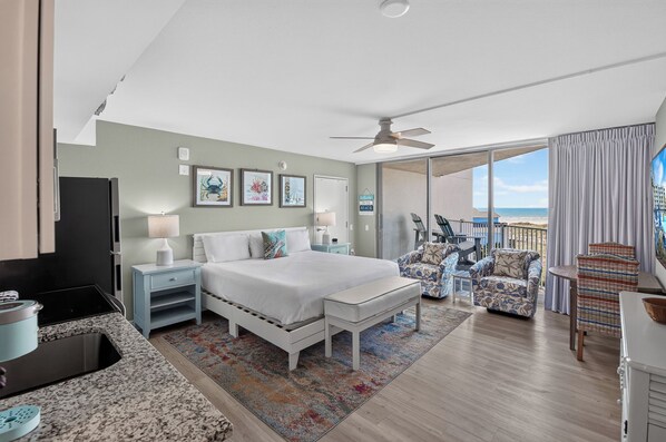 Une chambre d’hôtel comprenant un lit, un bureau, une chaise, un balcon avec vue sur la plage et un ventilateur de plafond.